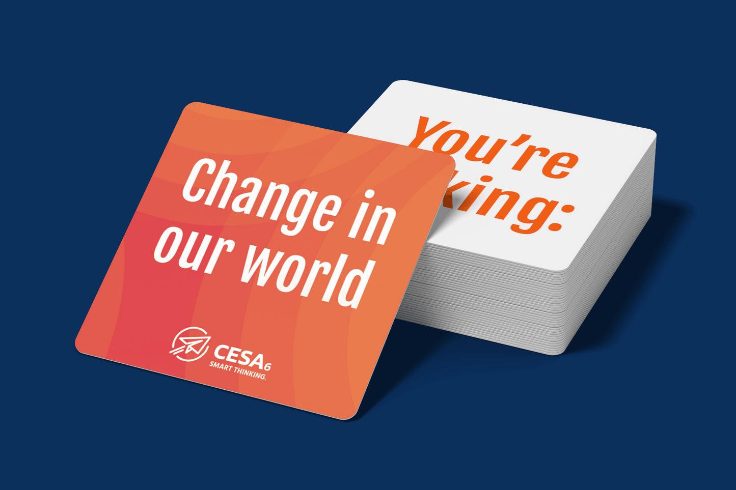A stack of square affirmation cards with rounded corners, resting on a dark blue background. The top card in the foreground is orange with white text that reads “Change in our world,” along with the CESA 6 logo and tagline “SMART THINKING.” A partially visible card in the background shows bold orange text on a white surface that reads, “You’re making:”.