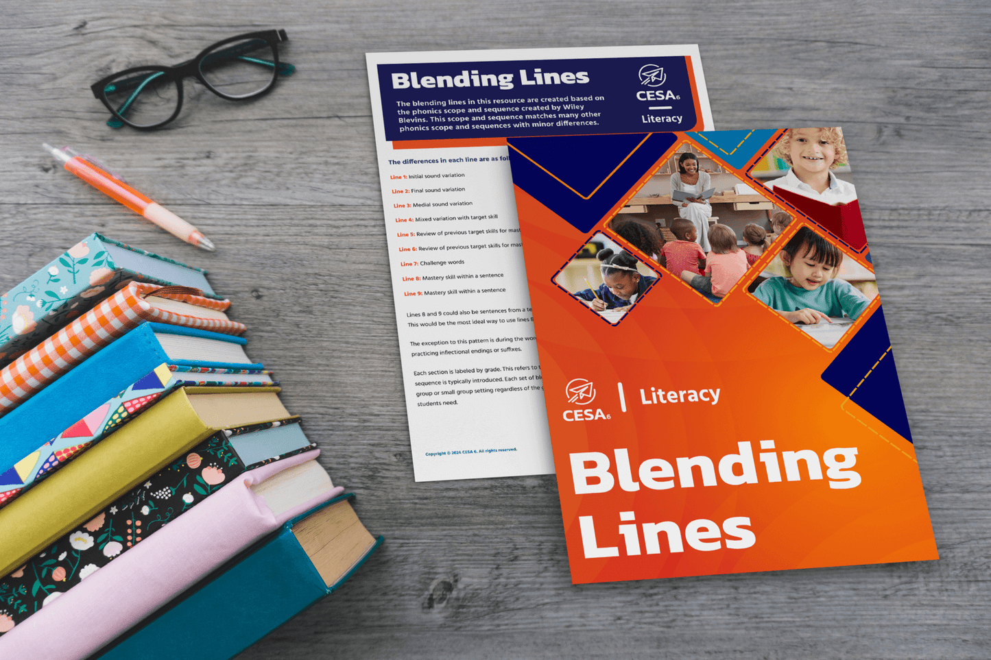 A stack of colorful books next to a printed "Blending Lines" resource guide, with a CESA6 Literacy cover and instructions for phonics practice. A pair of glasses and a pen are also visible.