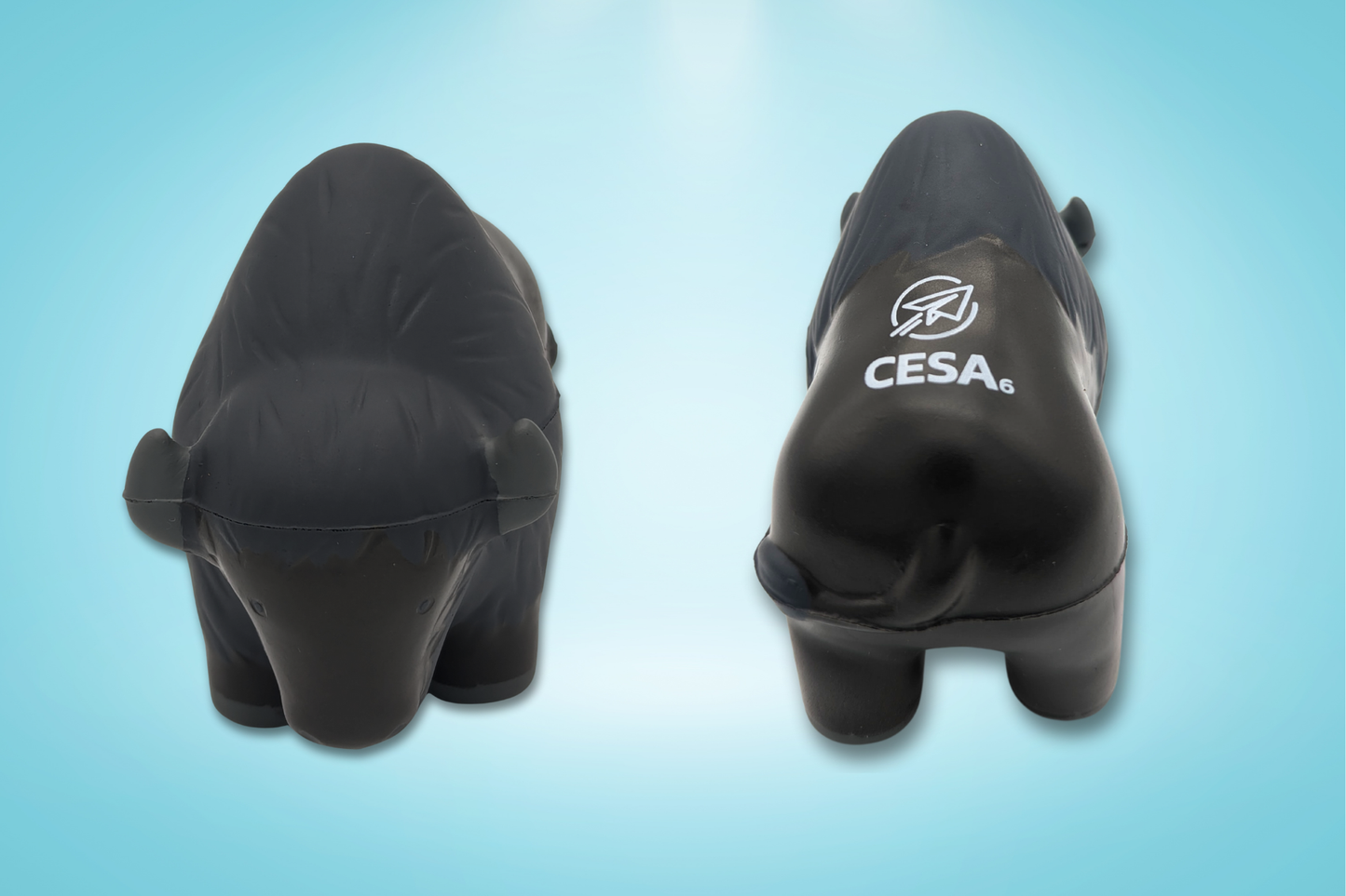 Image of a buffalo-shaped stress reliever toy shown from two angles on a light blue background. The left side displays a front view of the buffalo, with small ears and simple facial features. The right side shows a back view with the white CESA 6 logo printed on its back. The toy has a smooth, matte surface with subtle molded texture to represent fur.