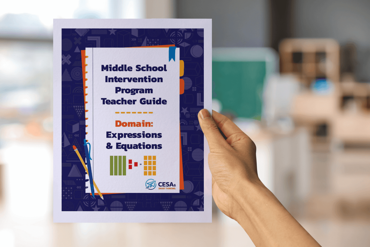 A hand is holding a booklet titled Middle School Intervention Program Teacher Guide: Domain: Expressions & Equations. The cover is decorated with math-themed icons along the border and shows visuals of algebra tiles representing expressions. The CESA 6 logo appears at the bottom. In the background, a blurred classroom with desks and shelves is visible.