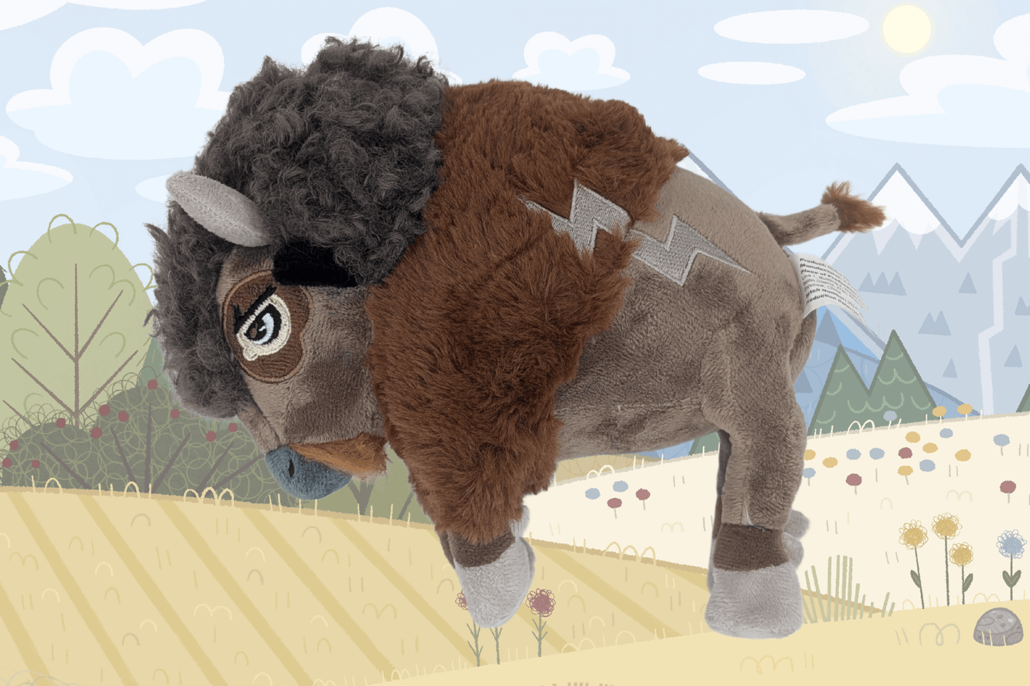 A plush buffalo toy named Duke is featured in the center of the image, set against a softly illustrated background of fields, trees, and snowy mountains under a bright sky. Duke has textured brown and gray fur with a fluffy mane, light gray hooves, and a lightning bolt-shaped patch on his side. He has a determined expression with stitched eyes.