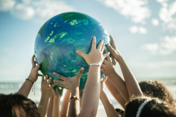 A group of diverse hands reaching up and holding a globe against a sunny beach backdrop.