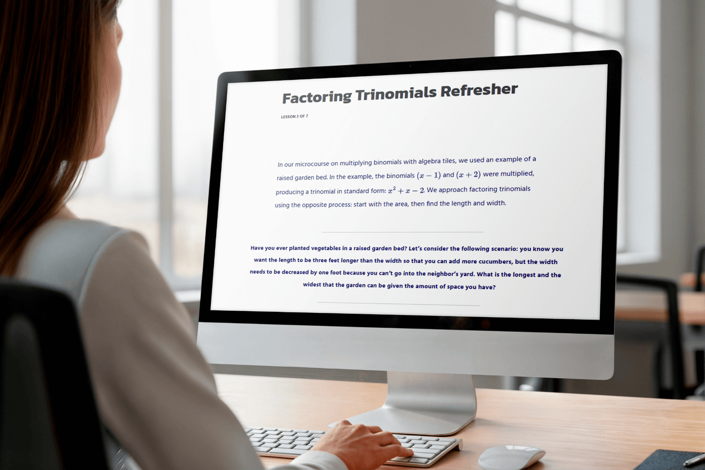 A person at a desk views a computer screen displaying "Factoring Trinomials Refresher," featuring text instruction on algebraic concepts.