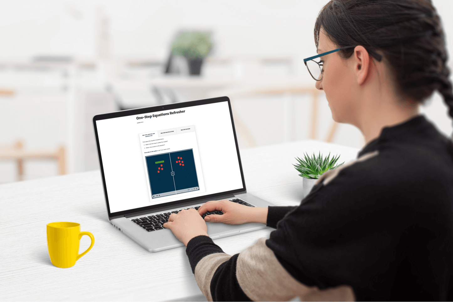 A woman sits at a white desk using a laptop displaying a "One-Step Equations Refresher." A bright yellow mug and a small plant are nearby, creating a focused and calm atmosphere.