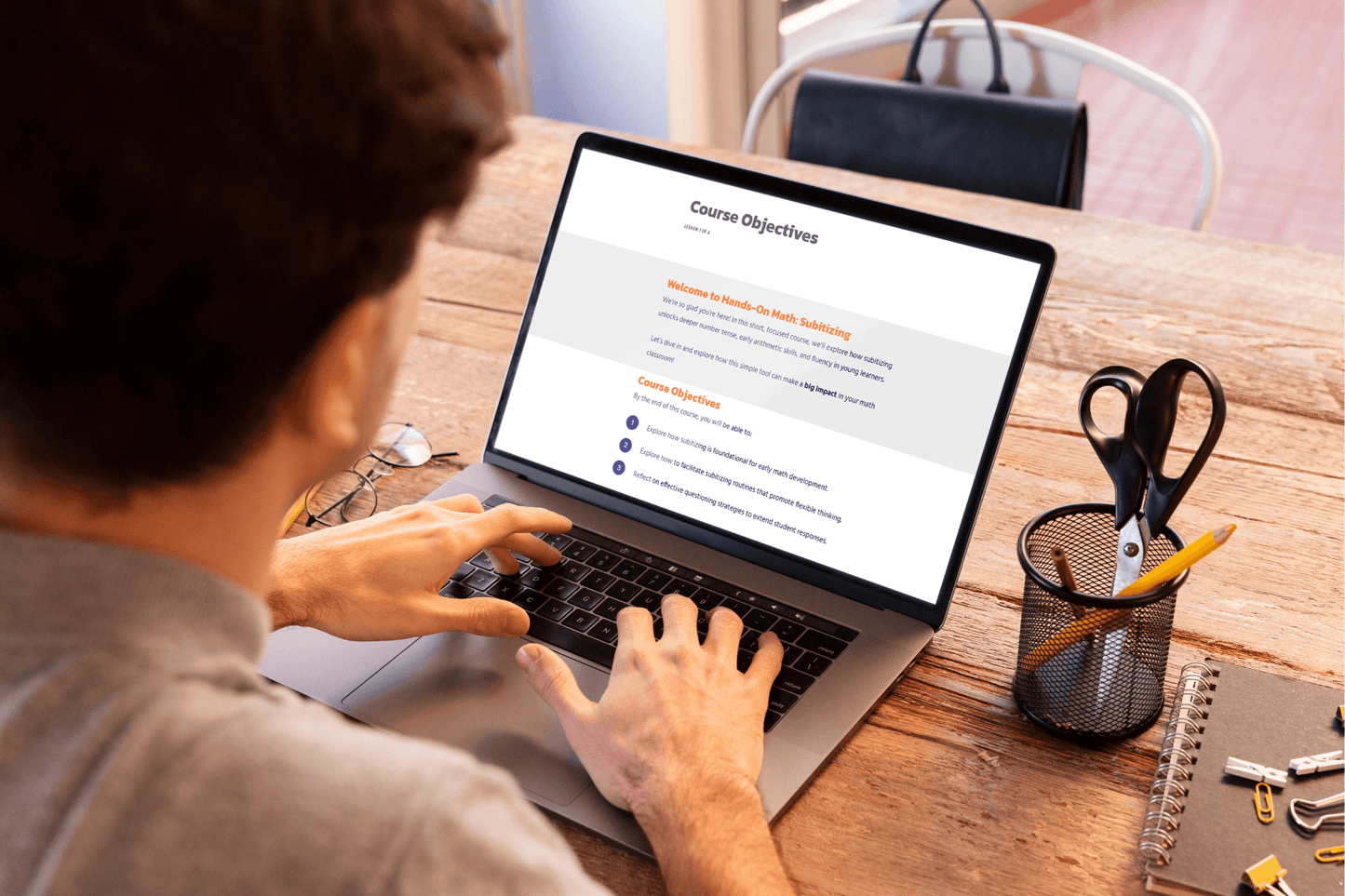 A person is working on a laptop displaying "Course Objectives." The setting is a wooden desk with stationery, conveying a focused, educational tone.