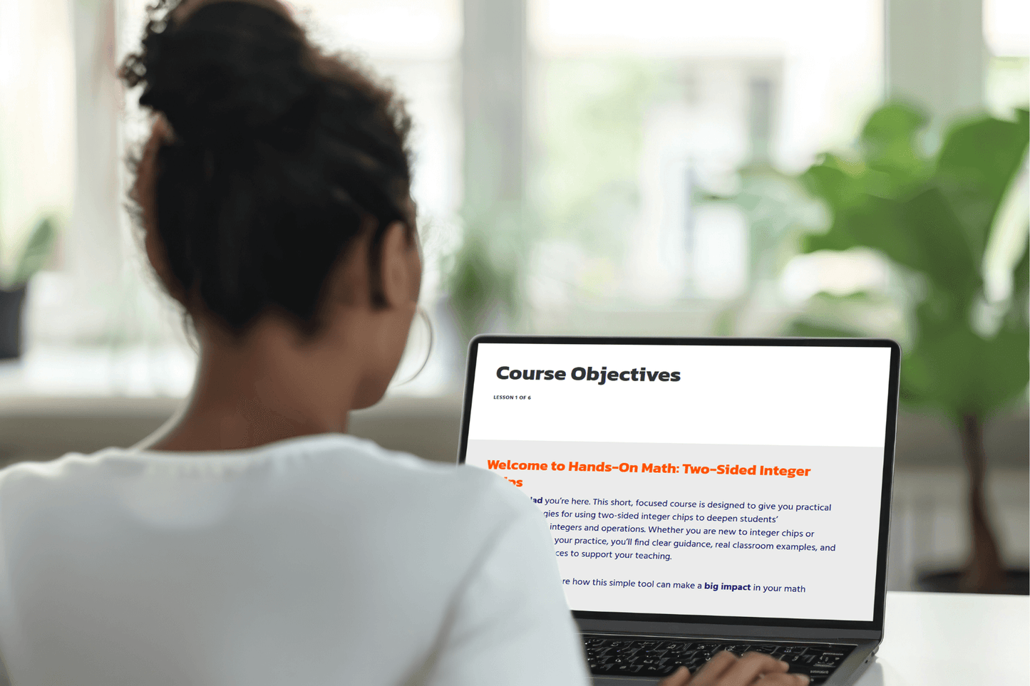 A person with a bun is using a laptop in a bright room. The screen displays a section titled "Course Objectives" for a math course. The scene is focused and studious.