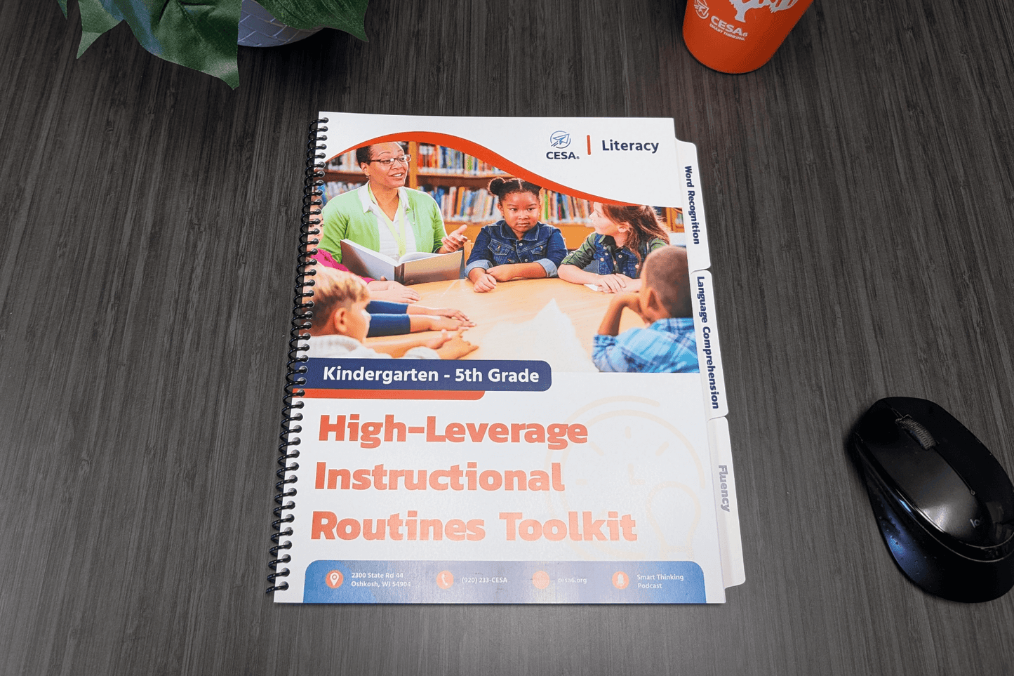 A spiral-bound educational toolkit on a desk. The cover features a teacher and children at a table, titled "High-Leverage Instructional Routines Toolkit."