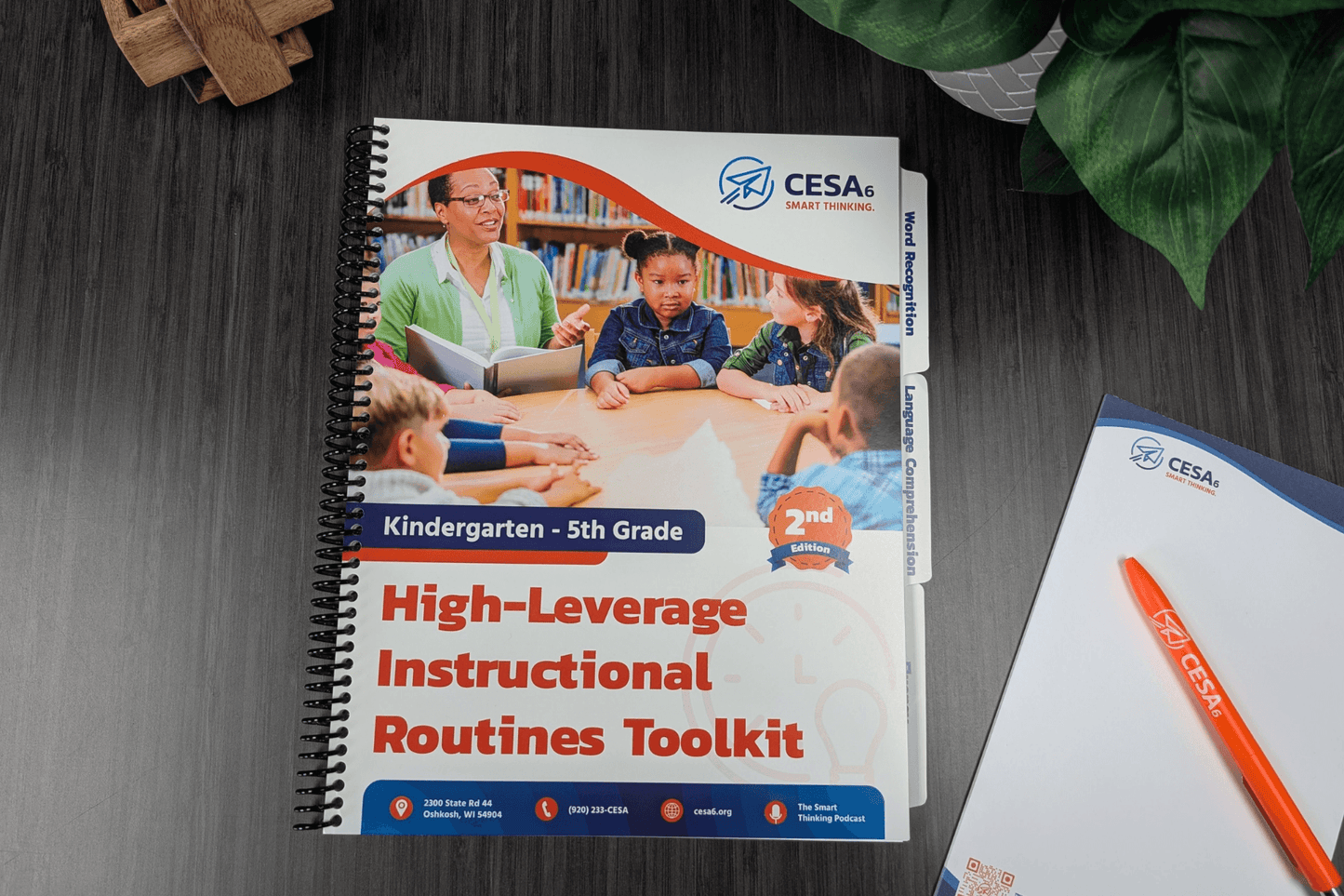 A spiral-bound educational toolkit on a desk. The cover features a teacher and children at a table, titled "High-Leverage Instructional Routines Toolkit."