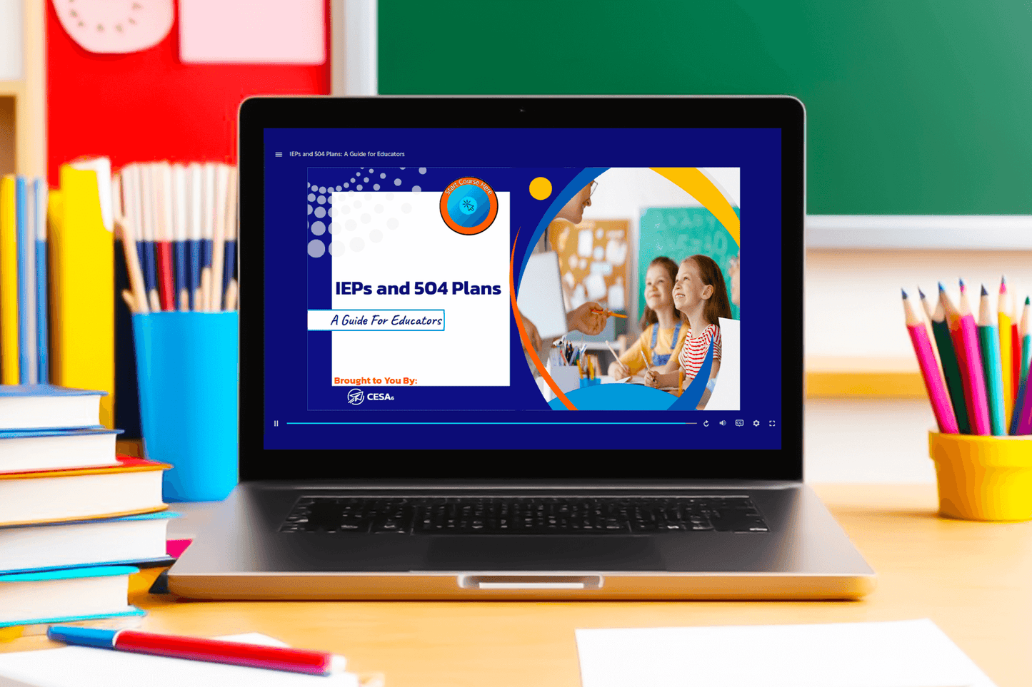 A laptop sits on a classroom desk with the screen displaying an educational slide titled “IEPs and 504 Plans: A Guide for Educators.” The slide features a modern design with blue, orange, and white accents. On the right side of the slide is a circular image of a teacher smiling at two young students in a classroom. The content is labeled "Brought to You By: CESA 6." Around the laptop are colorful school supplies.