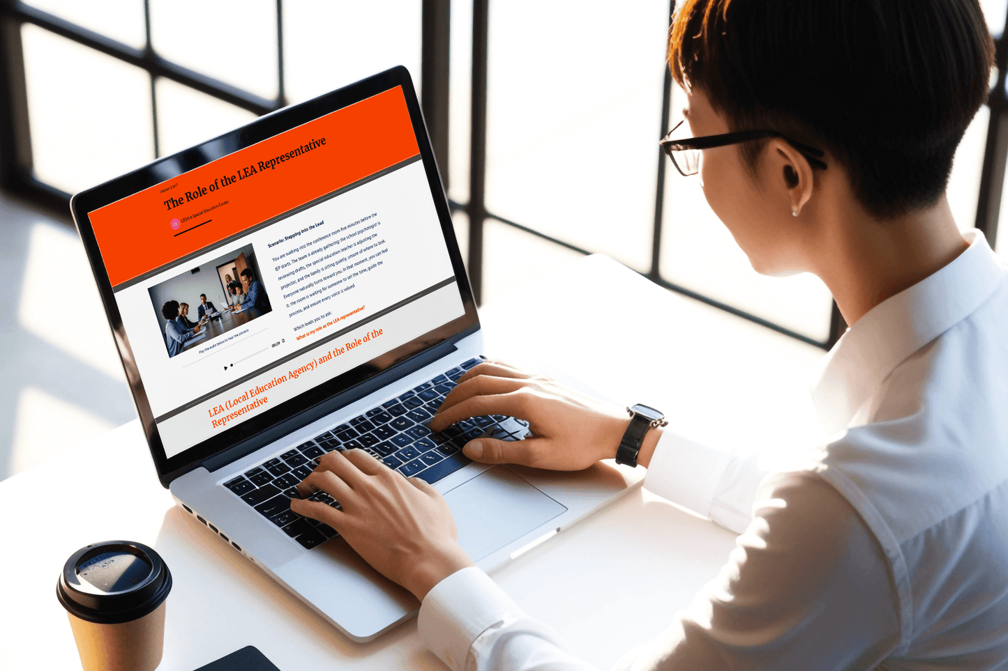 A person wearing glasses works on a laptop displaying an article titled "The Role of the LEA Representative." Sunlight streams through a window, creating a focused, professional ambiance.