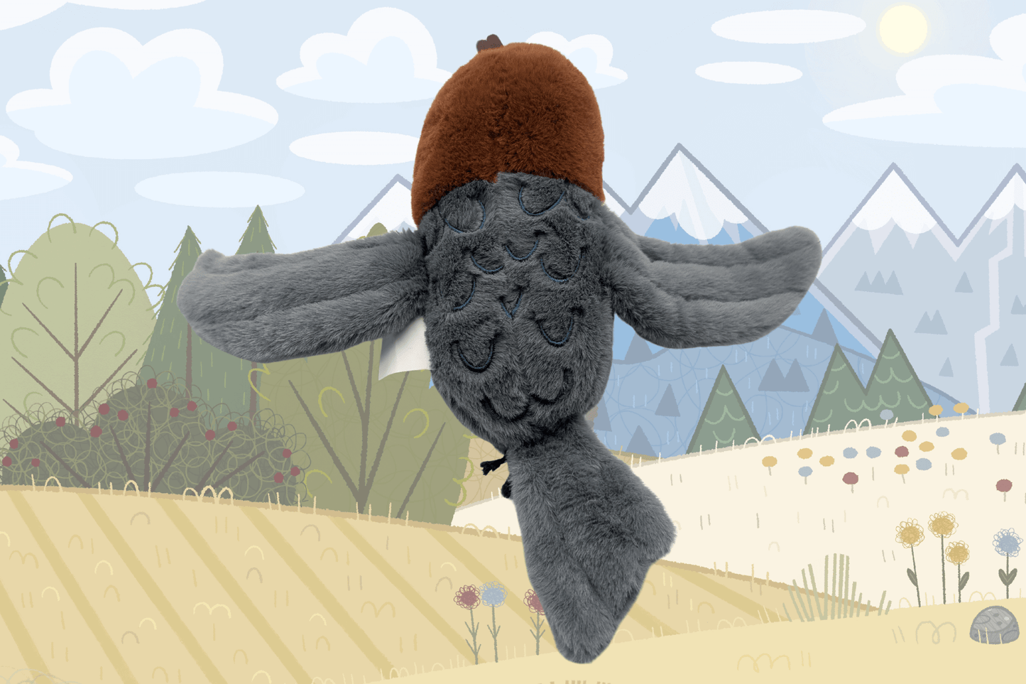 This image shows the back view of a plush bird named Tootsie, posed against an illustrated background of trees, fields, and mountains. The plush has a rust-colored head and a dark gray body with wide outstretched wings. The back features stitched feather patterns in dark blue thread. The plush tail and wings are fluffy and soft, and a white tag is partially visible along the side.