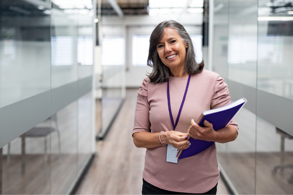 Female teacher holding a blue folder in an office hallway