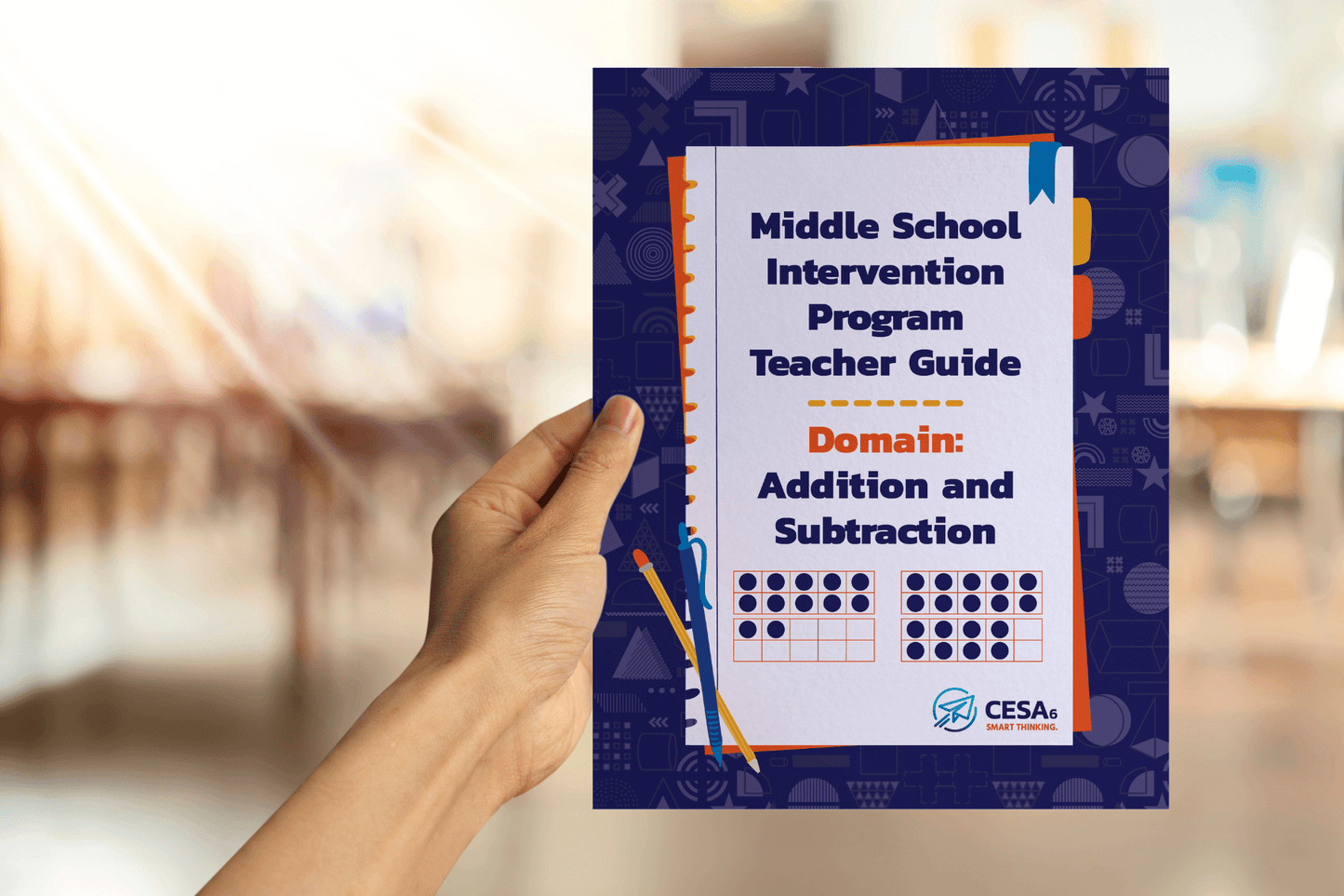 A hand holds a "Middle School Intervention Program Teacher Guide" for addition and subtraction. The background is a blurred classroom.