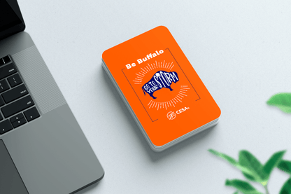 A "Be Buffalo" card deck by CESA6 is placed next to a laptop on a desk with a small plant in the background.