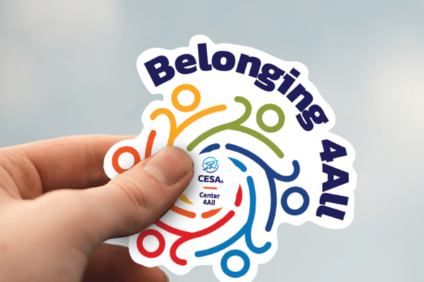 A hand holding a "Belonging 4ALL" sticker, featuring colorful, diverse figures in a circular design with the CESA6 Center 4All logo.