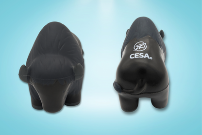 Image of a buffalo-shaped stress reliever toy shown from two angles on a light blue background. The left side displays a front view of the buffalo, with small ears and simple facial features. The right side shows a back view with the white CESA 6 logo printed on its back. The toy has a smooth, matte surface with subtle molded texture to represent fur.