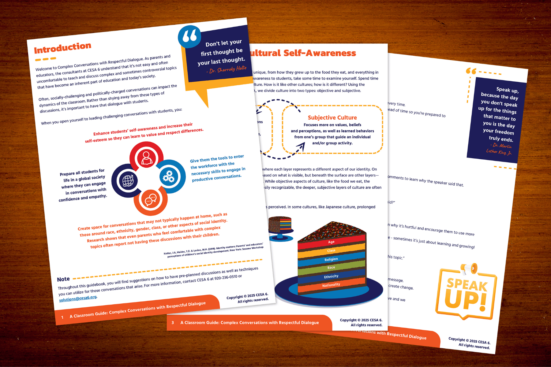Three educational pamphlets with colorful graphics on cultural awareness and dialogue are spread across a wooden table. They feature quotes, charts, and icons.
