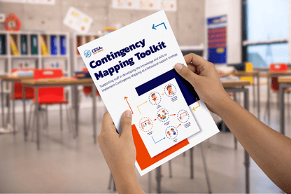 Hands holding a "Contingency Mapping Toolkit" booklet in a classroom. The cover shows diagrams and text in a colorful, professional design.