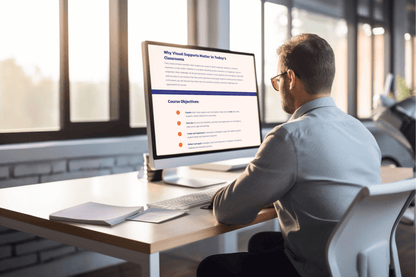 Man in an office setting working on a computer. The screen displays an educational text about visual supports in classrooms. Natural light filters through large windows.