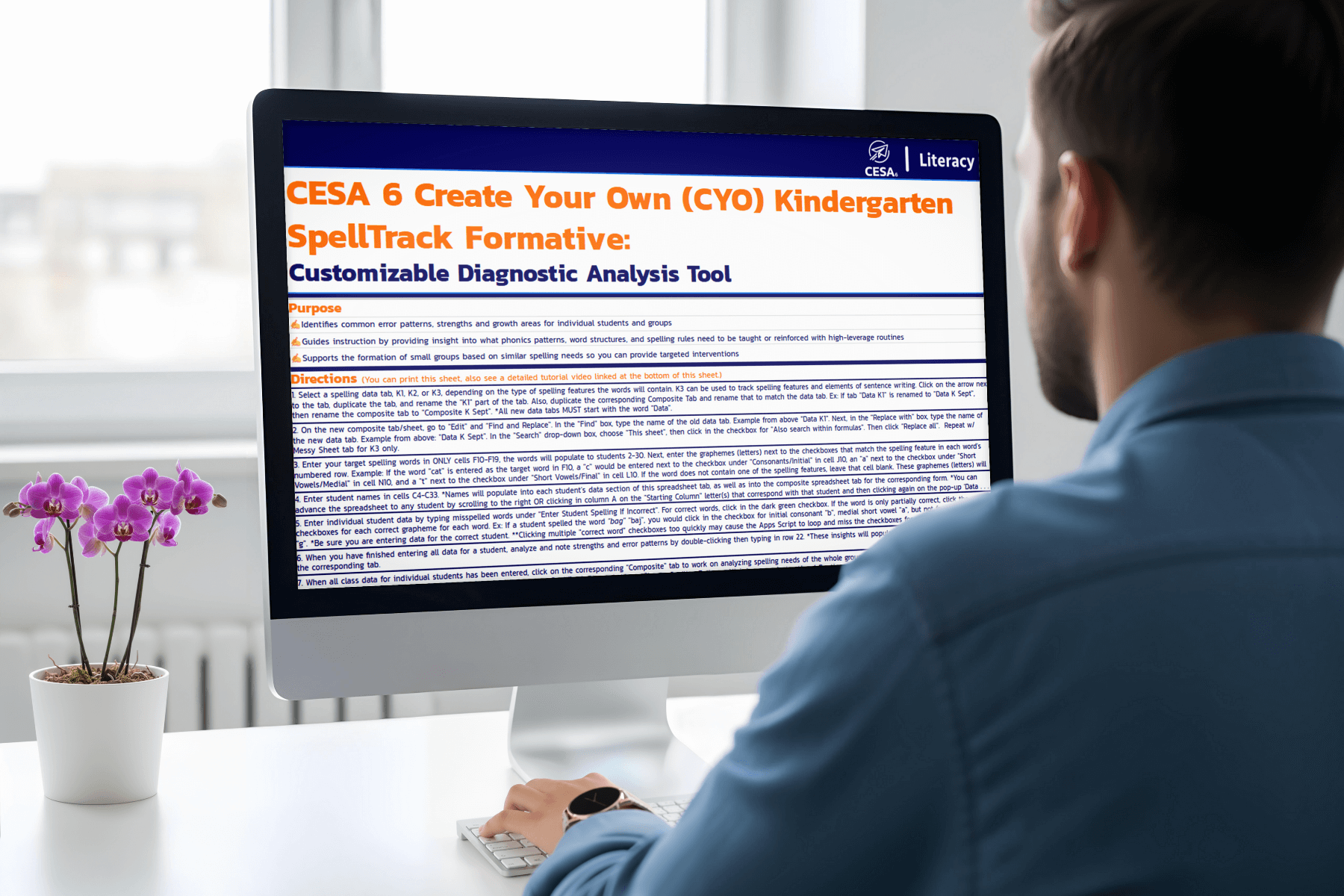 A person in a blue shirt views a computer monitor displaying a detailed educational tool titled "CESA 6 Create Your Own Kindergarten SpellTrack Formative." Nearby, a small plant adds a touch of color.