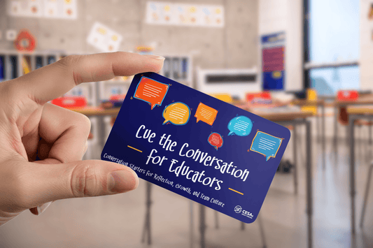 A hand holds a card with colorful speech bubbles and text: "Cue the Conversation for Educators." Blurred classroom background.