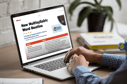 A person in a checkered shirt watches a YouTube video titled "New Multisyllabic Word Routine" on a laptop, with books and a plant nearby.