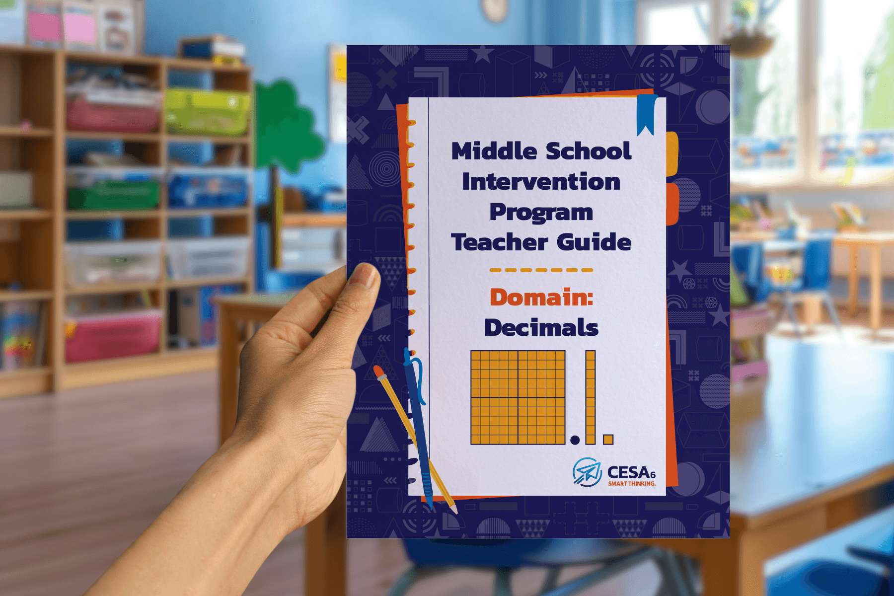 A hand holds a guide titled "Middle School Intervention Program Teacher Guide: Domain Decimals" with educational graphics. A classroom is blurred in the background.