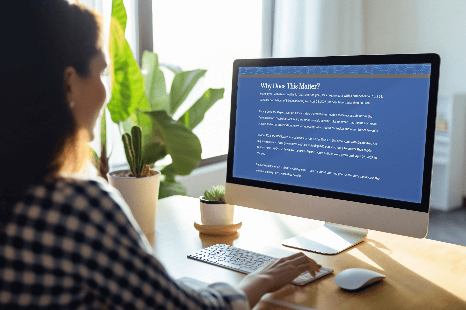 A person in a checkered shirt is sitting at a desk, viewing a computer screen displaying a webpage titled "Why Does This Matter?" Sunlit room with plants.