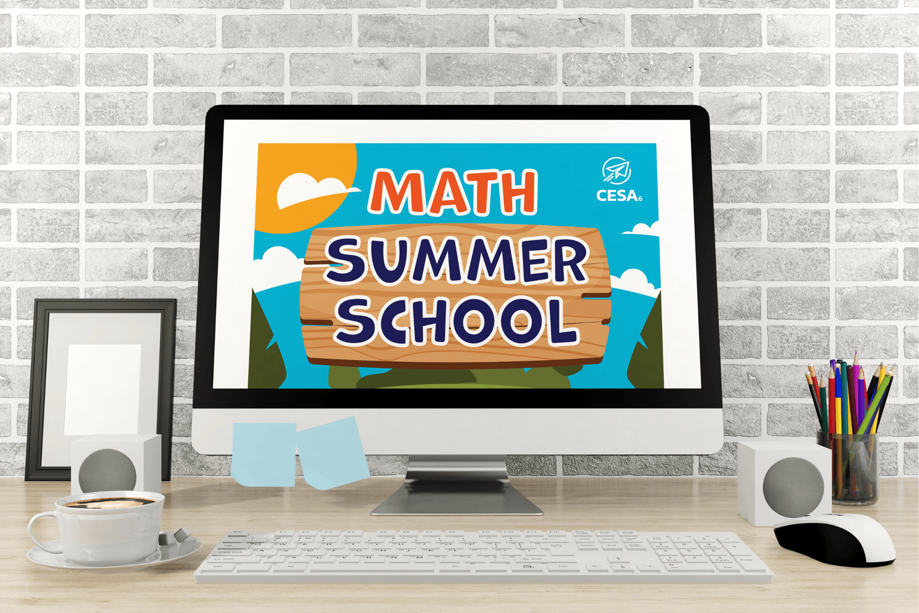 Computer screen showing "Math Summer School" with colorful block letters. Desk includes speakers, a cup of coffee, pencils in a holder, and sticky notes, evoking an educational and inviting atmosphere.