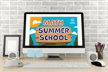 Computer screen showing "Math Summer School" with colorful block letters. Desk includes speakers, a cup of coffee, pencils in a holder, and sticky notes, evoking an educational and inviting atmosphere.