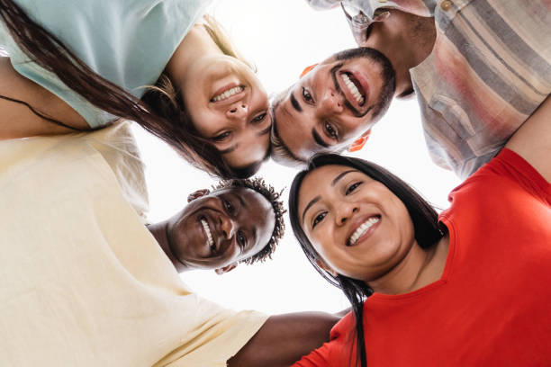 A diverse group of five people smiling and standing in a circle, looking down at the camera from below.