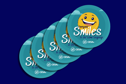 A set of five identical round stickers features a smiling yellow face in the center. Around it is a teal background with the phrase “Everyone Smiles in the same language.” written in playful white and navy lettering, along with the CESA 6 logo at the bottom.