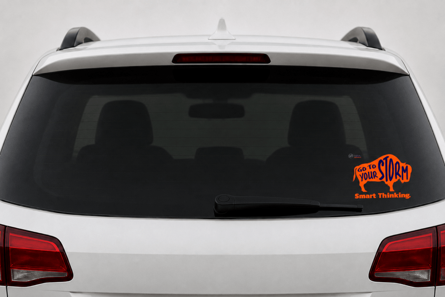 Rear view of a white SUV with a transparent static cling displayed on the lower right corner of the rear window. The cling features an orange buffalo with the words "GO TO YOUR STORM" in dark blue, the phrase "Smart Thinking." in orange, and the CESA 6 logo.