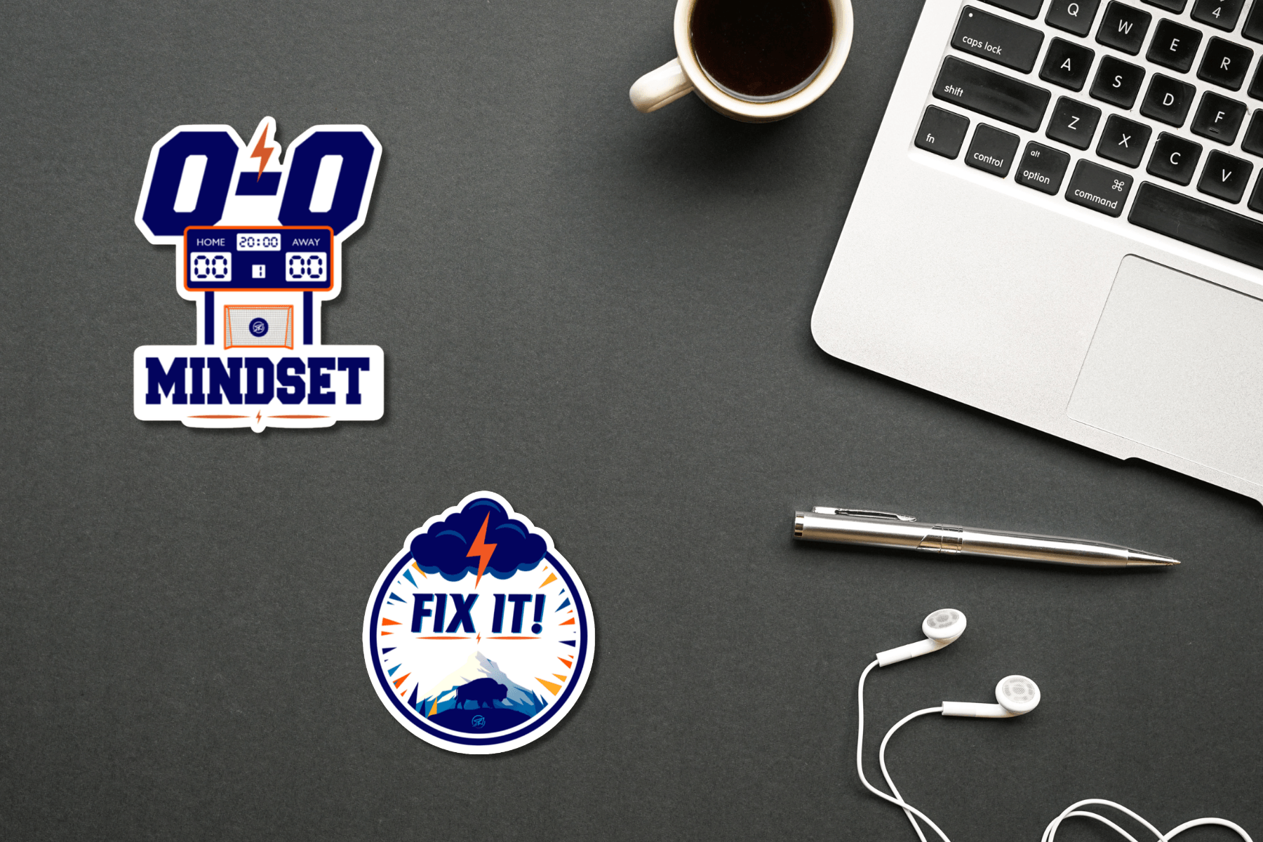 Two motivational leadership stickers displayed on a dark desk beside a laptop, coffee cup, pen, and earbuds. One sticker features a 0–0 scoreboard with the words “0-0 Mindset,” while the other features a storm cloud, lightning bolt, mountains, and buffalo with the words “Fix It!”