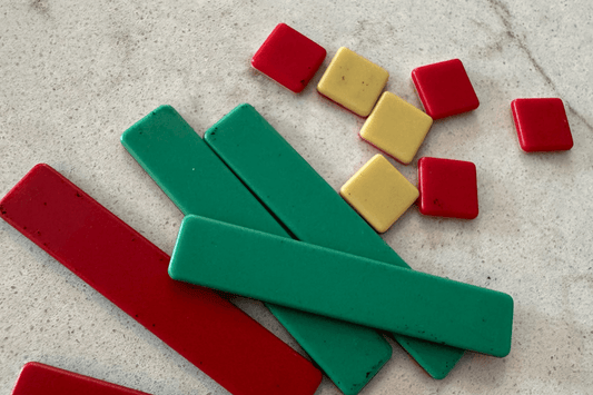Colorful geometric blocks on a light surface: three red and three green rectangles overlap, next to small red and yellow squares scattered above.