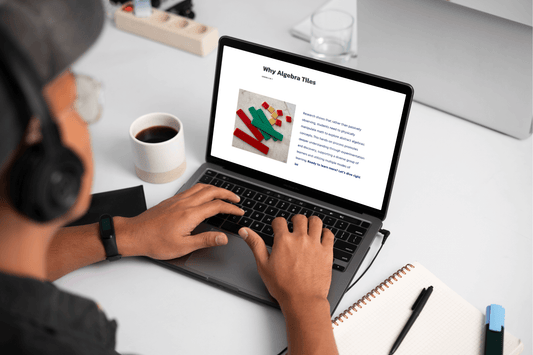 A person wearing headphones types on a laptop displaying an article titled "Why Algebra Tiles." A notebook, pen, and coffee cup are on the desk.