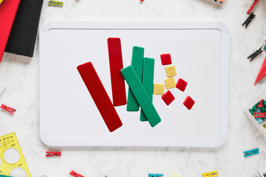 Colorful geometric shapes, including red and green rectangles and small red and yellow squares, are arranged on a whiteboard. The background has scattered stationery items, creating a playful and creative atmosphere.