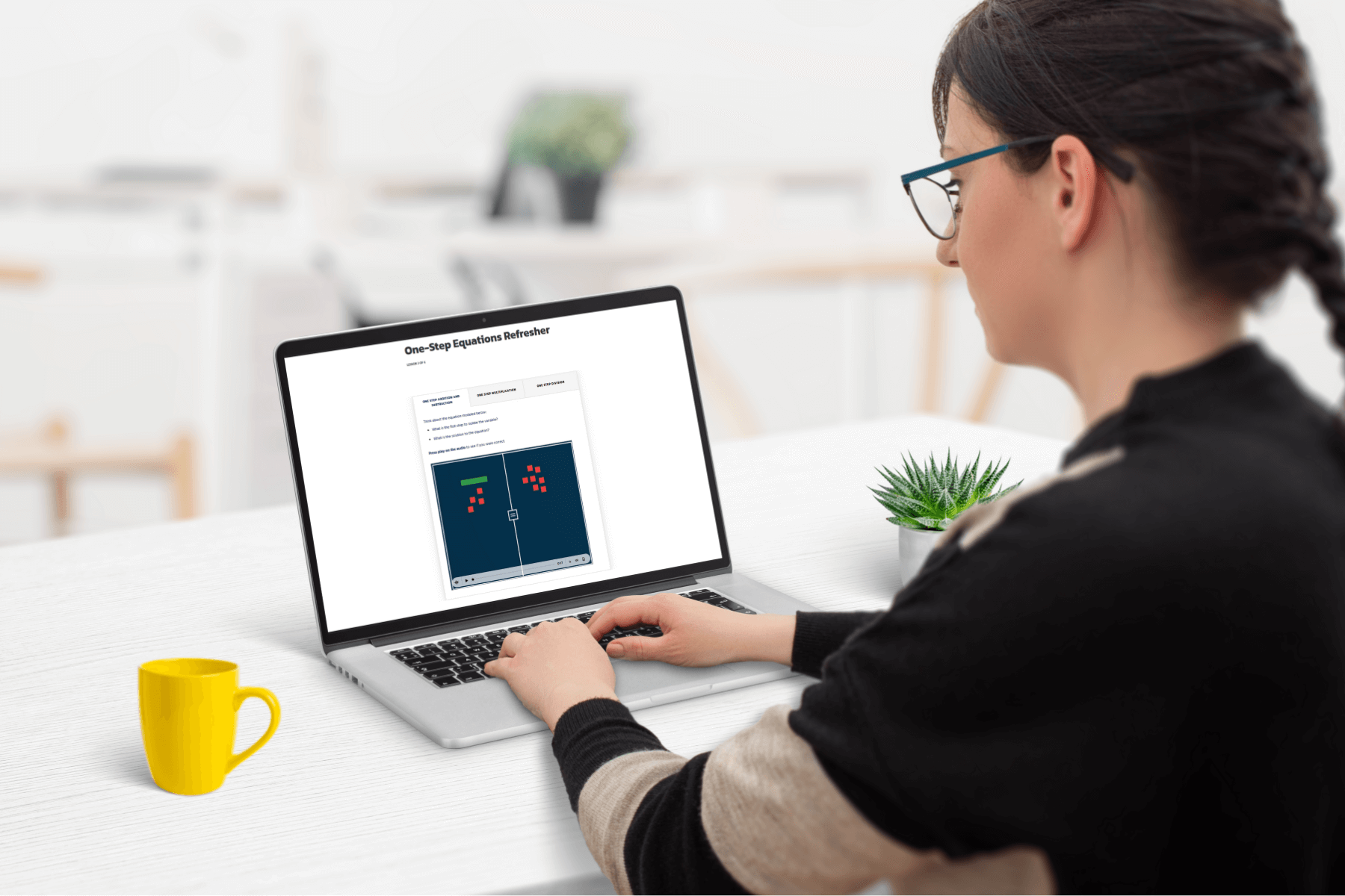 A woman sits at a white desk using a laptop displaying a "One-Step Equations Refresher." A bright yellow mug and a small plant are nearby, creating a focused and calm atmosphere.