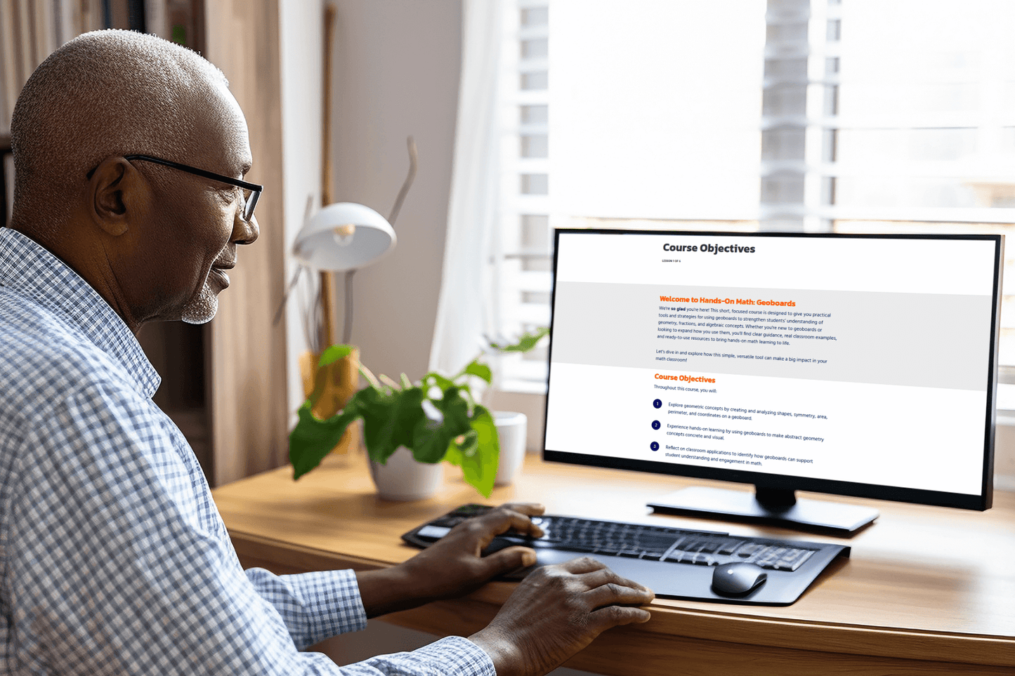 A person in glasses sits at a wooden desk, focused on a computer screen displaying course objectives. A plant and soft lighting create a calm workspace.