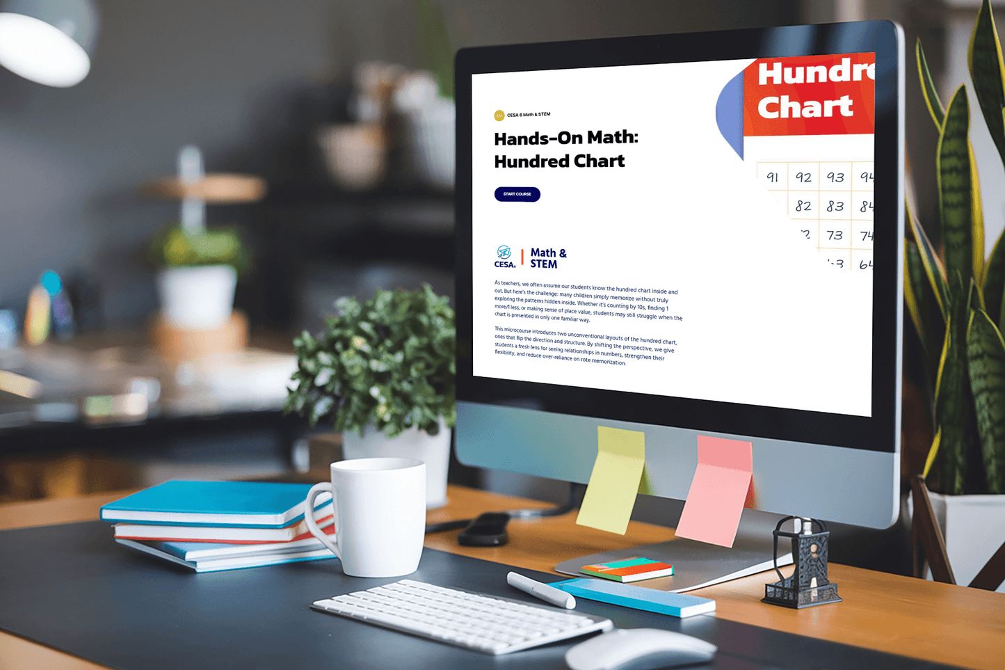 A desk with a computer displaying a webpage titled "Hands-On Math: Hundred Chart." Desk items include a plant, books, a mug, and colorful sticky notes.