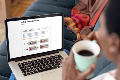 Person holding a mug while viewing a math lesson on a laptop, focused on using a number rack. Cozy, engaged learning atmosphere.