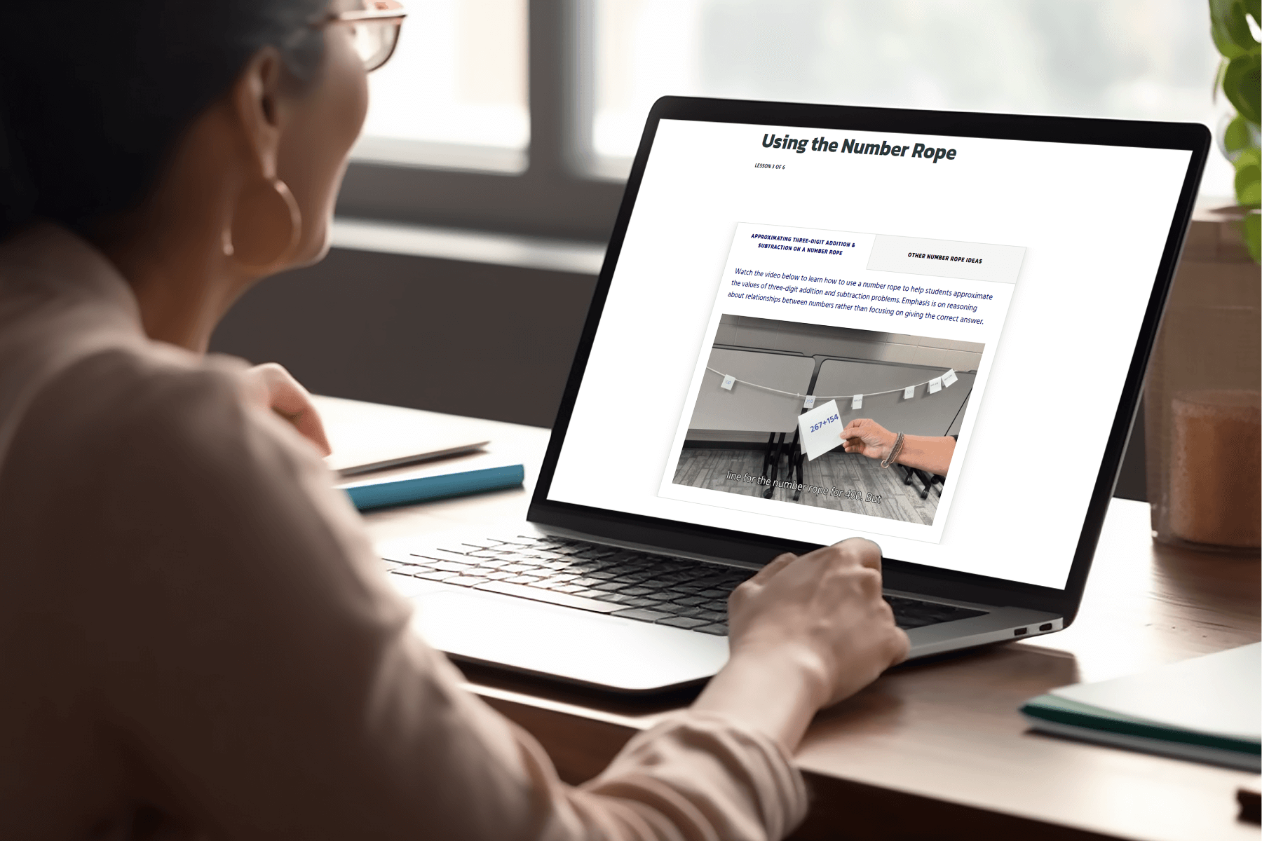 A person with glasses is sitting at a desk, looking at a laptop screen displaying an lesson titled "Using the Number Rope," focused on education.