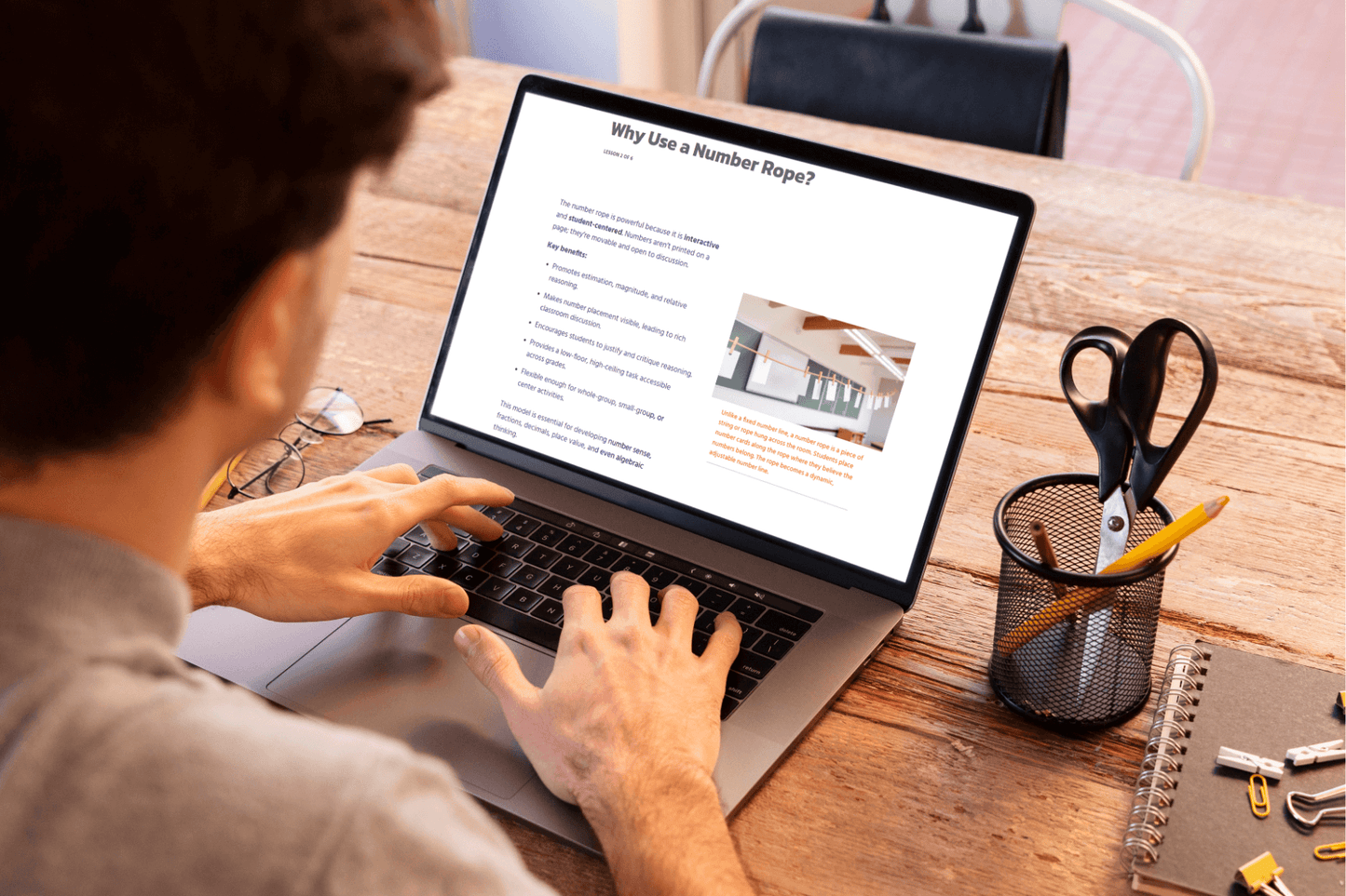 A person interacting with the lesson titled "Why Use a Number Rope?" The setup is on a wooden desk with a pen holder and a notebook, creating a focused, studious atmosphere.