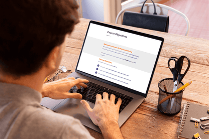 A person is working on a laptop displaying "Course Objectives." The setting is a wooden desk with stationery, conveying a focused, educational tone.