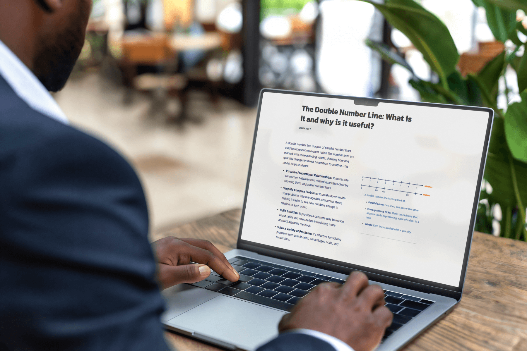 A person in a suit types on a laptop displaying a webpage titled "The Double Number Line: What is it and why is it useful?" in a modern office setting.