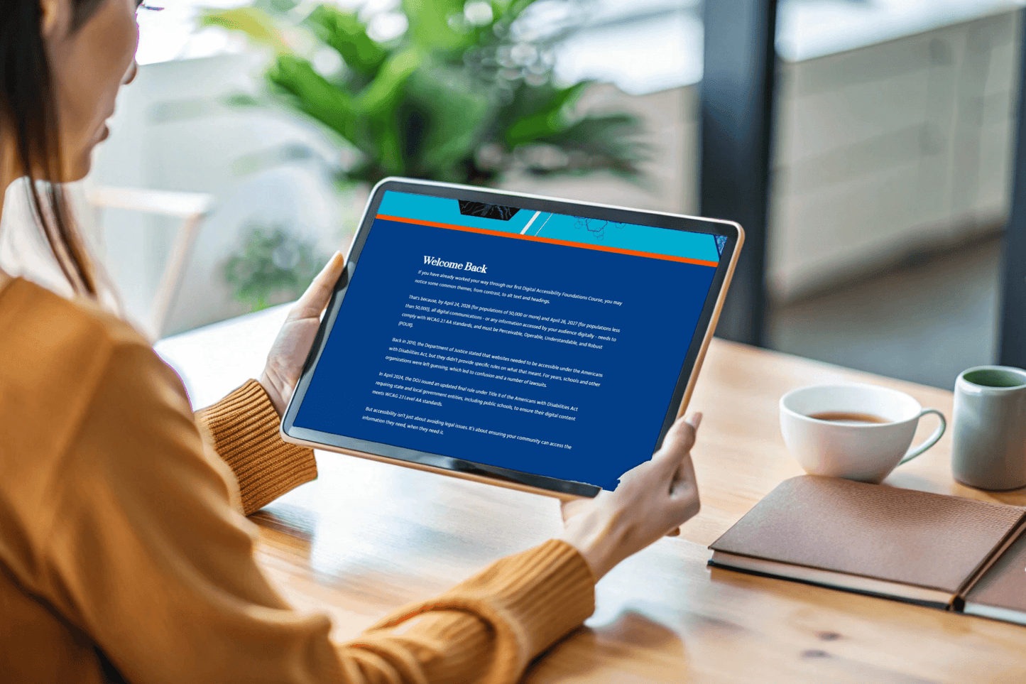 A woman in a cozy sweater holds a tablet displaying a "Welcome Back" message on a blue screen. A notebook and coffee mugs sit on the table, creating a warm atmosphere.