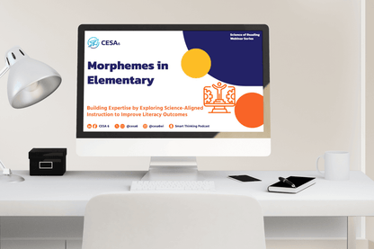 A computer screen displays a webinar slide titled "Morphemes in Elementary." The slide features blue and orange geometric shapes and educational graphics. A desk lamp, notebook, and mug are on the white table, creating a neat and professional setting.