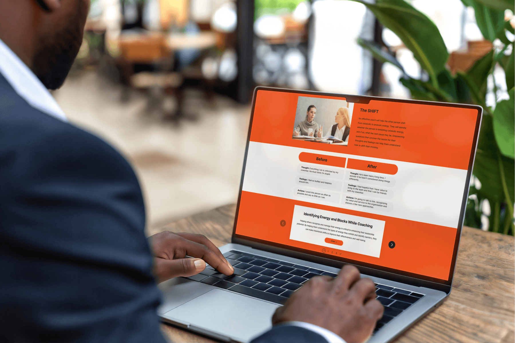 A person in a suit is using a laptop displaying a webpage with orange and white sections, featuring text and images. The atmosphere is focused.