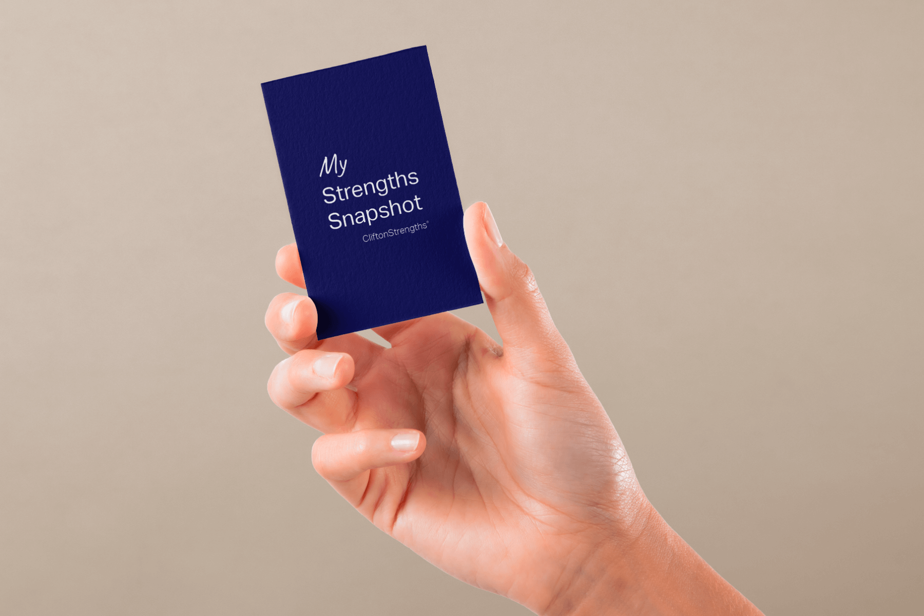 A hand holding a blue card that reads "My Strengths Snapshot, CliftonStrengths." The background is a neutral beige, conveying a calm and focused tone.