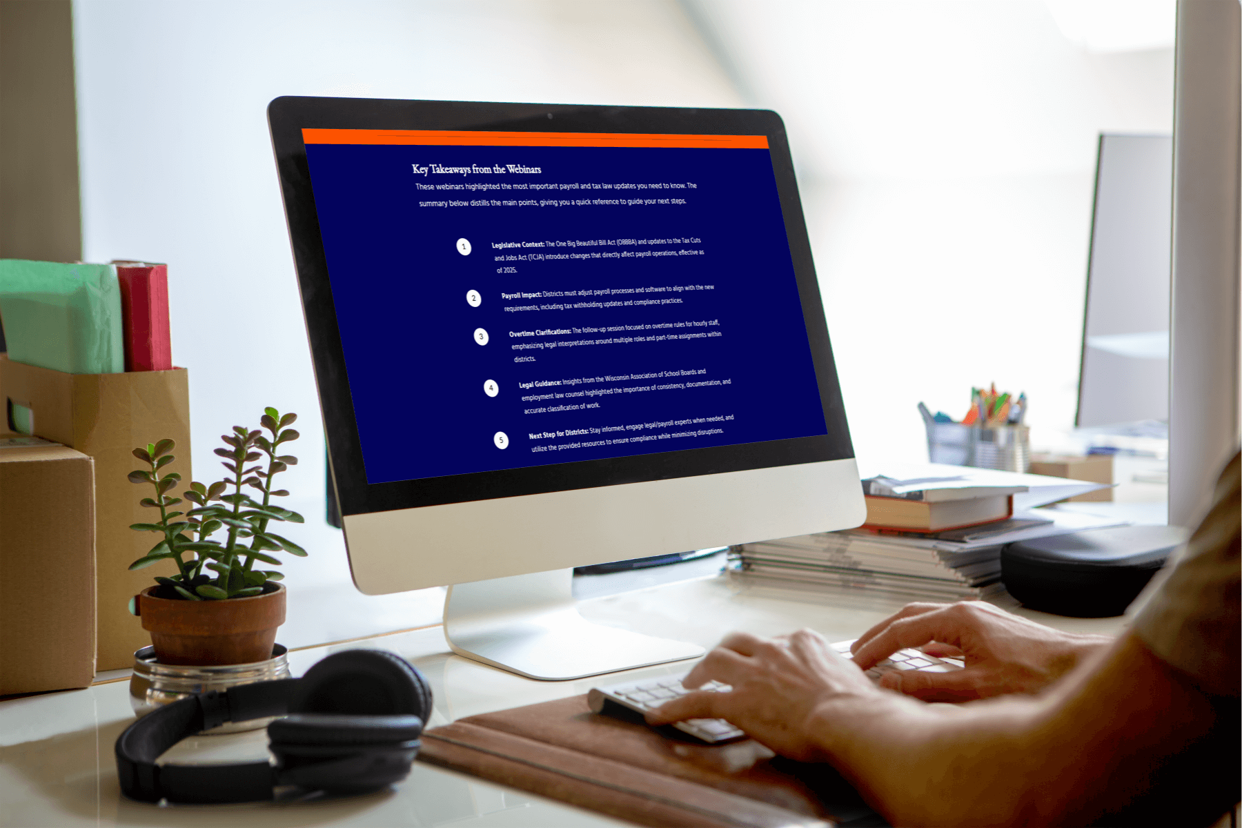A person works at a desktop computer displaying a training module slide titled “Key Takeaways from the Webinars.” The screen shows a list of five key points related to payroll and tax law updates, covering legislation context, payroll impact, overtime clarification, legal guidance, and next steps for districts. The workspace includes a plant, headphones, and stacked books on the desk, creating an organized office environment.